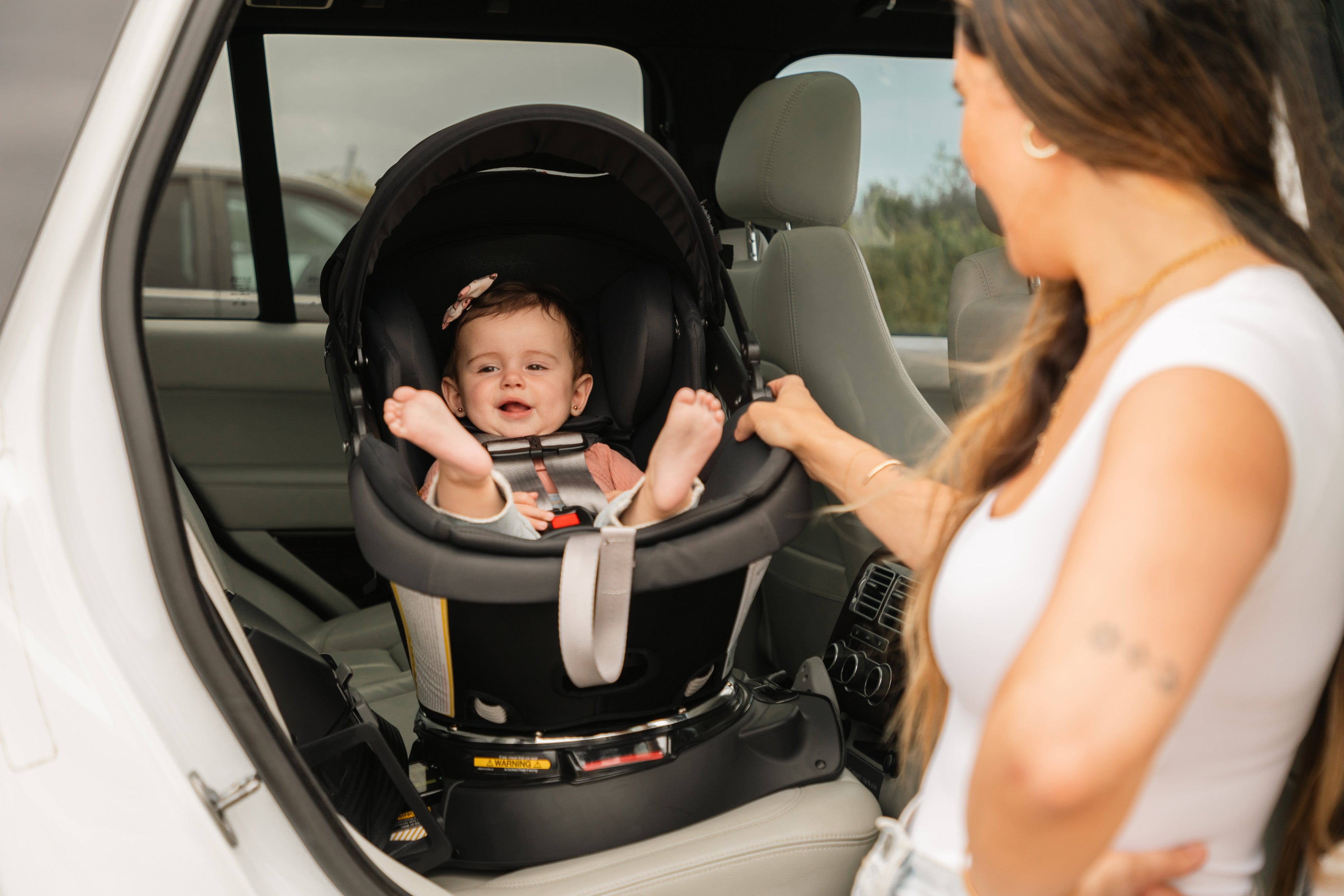 Baby in an Orbit Baby G5+ Infant Car Seat docked on its base inside a car, parent's hand on the handle